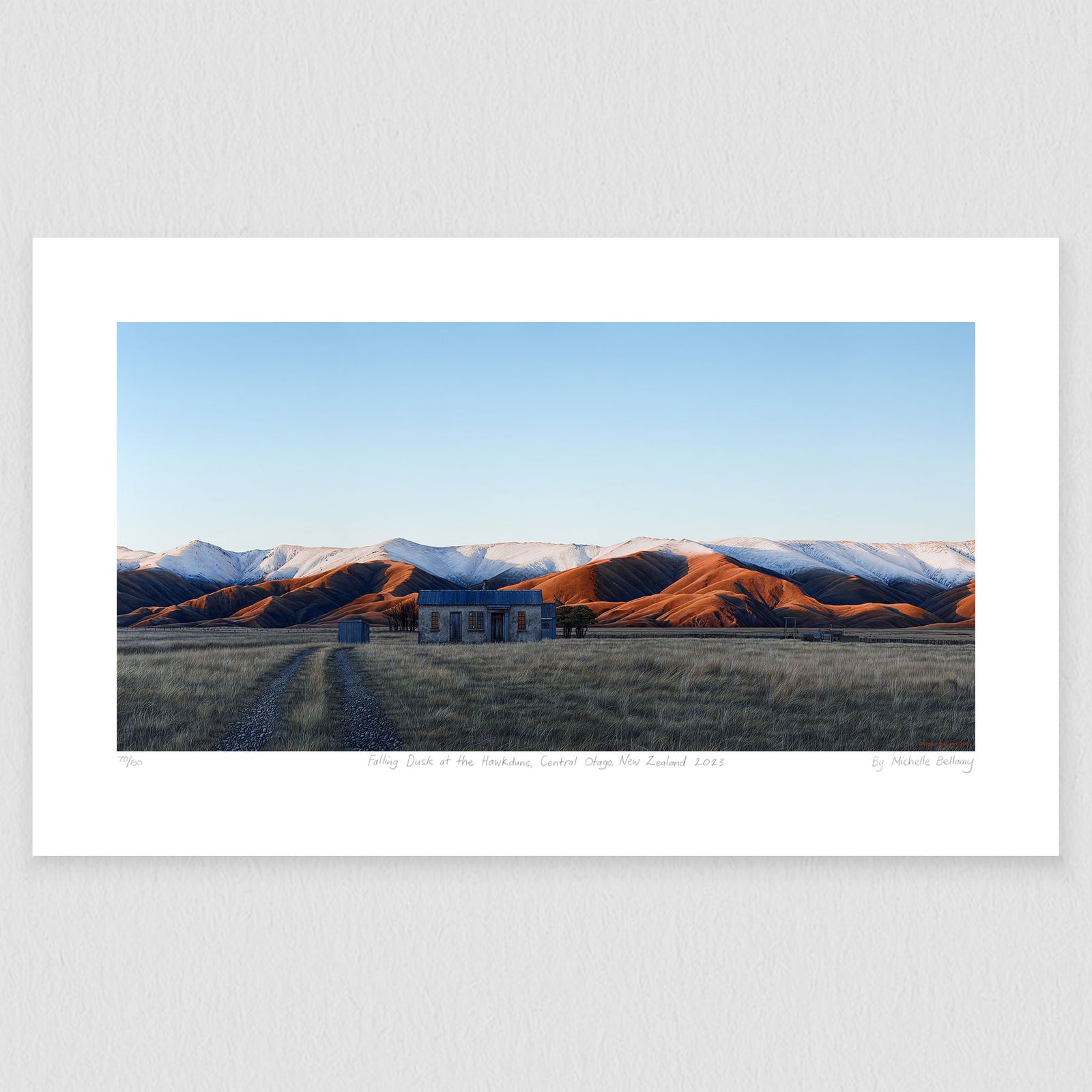A art print of the snowy Hawkdun range and a rustic building in the deep orange evening light in Central Otago.
