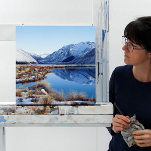 Artist Michelle Bellamy standing next to a landscape painting of Lake Tennyson in the Molesworth.