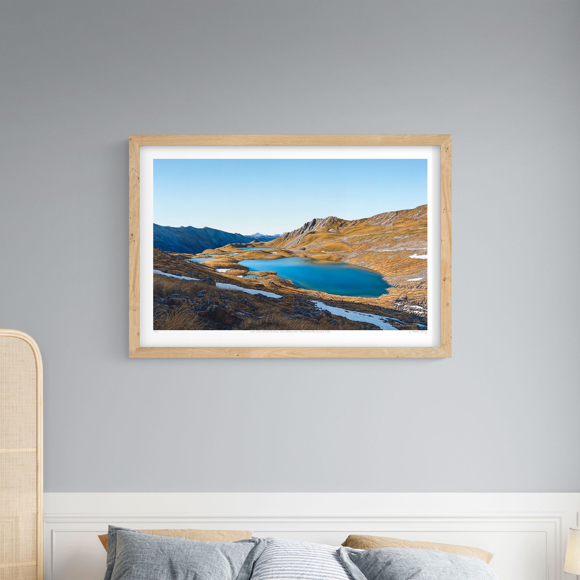 A framed landscape art print above a bed featuring the Paratītahi Tarns in the Saint Arnaud Range of the Nelson Lakes National Park, New Zealand.